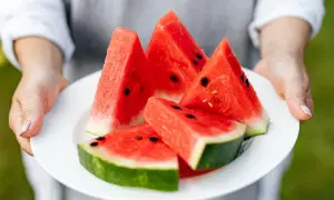 Kawałki soczystego arbuza na białym talerzu, trzymanym przez dłonie.
